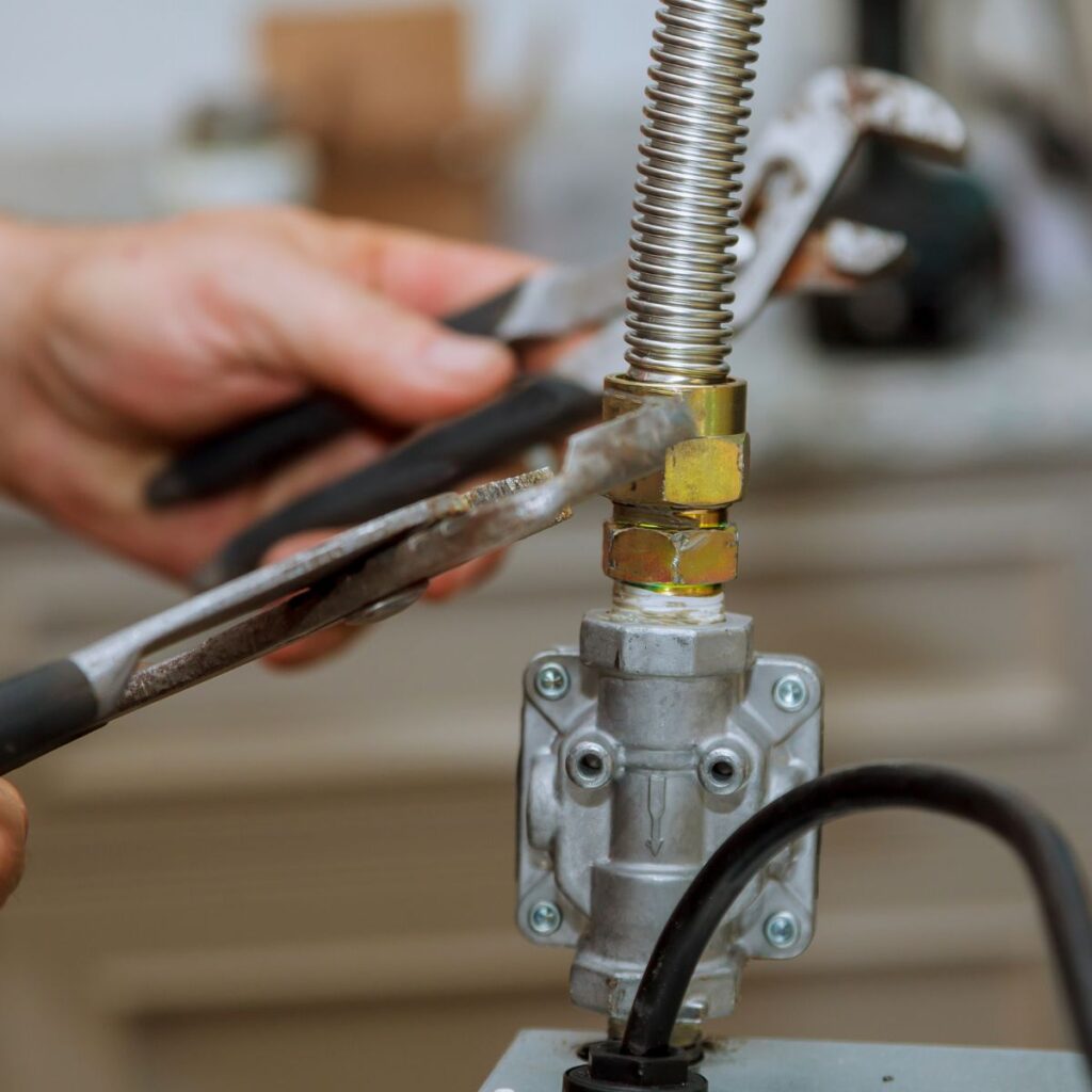 A person uses two wrenches to tighten a connection on a corrugated metal gas line attached to a silver valve