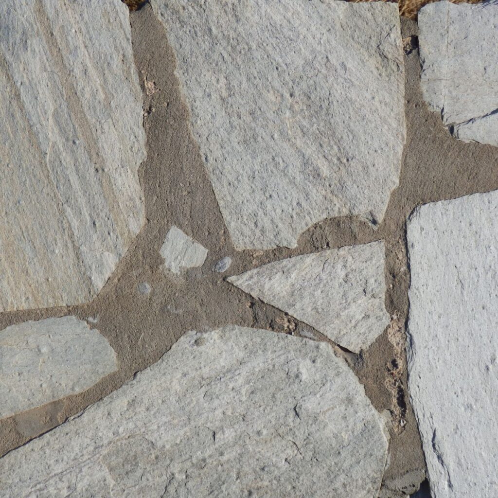 A close-up view of a flagstone patio shows irregular grey stones mortared together with dark grout