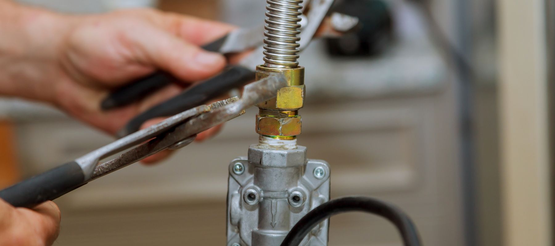 A person uses two wrenches to tighten a connection on a flexible corrugated metal gas line