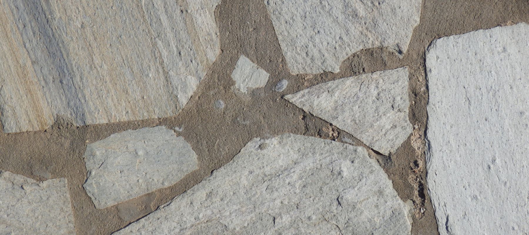 A close-up texture shot displays light-colored, irregularly shaped flagstones with dark gray grout lines