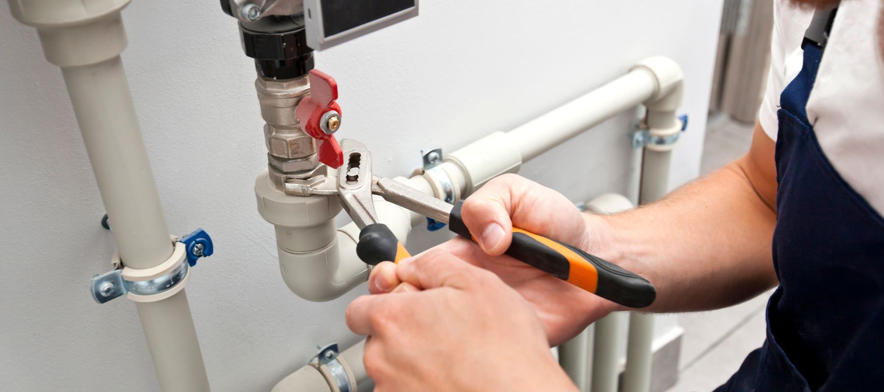 A plumber uses an adjustable wrench to tighten a valve on a white PVC pipe system with a red handle