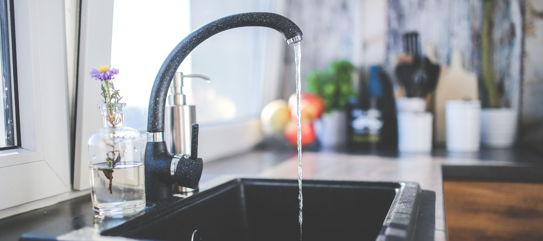 Kitchen sink faucet running water beside a small vase with a flower