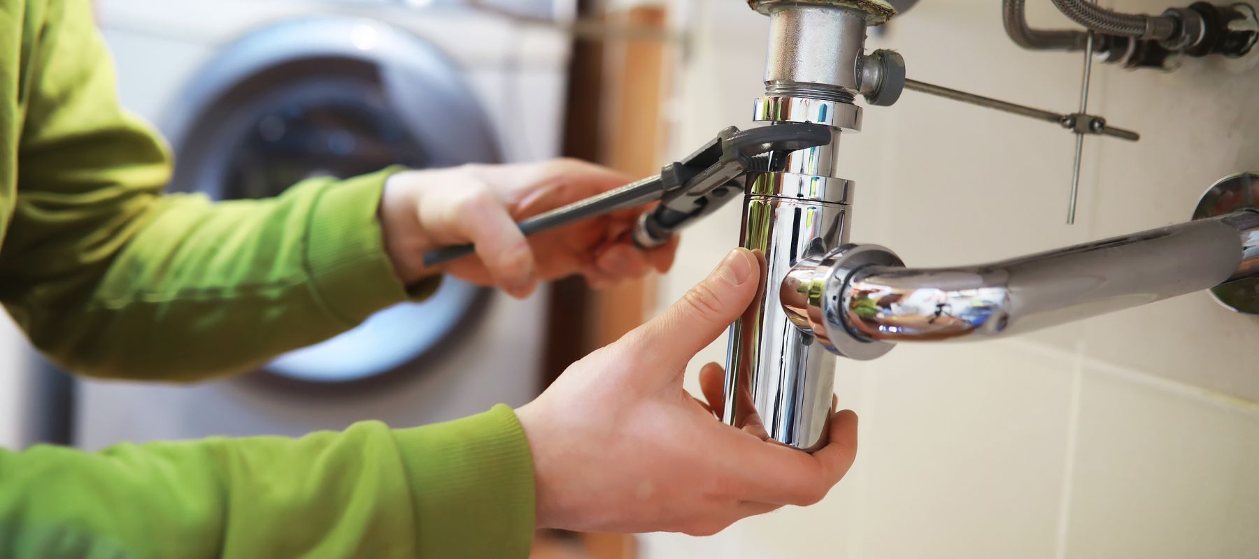 Plumber tightening a shiny chrome pipe under a sink with a wrench