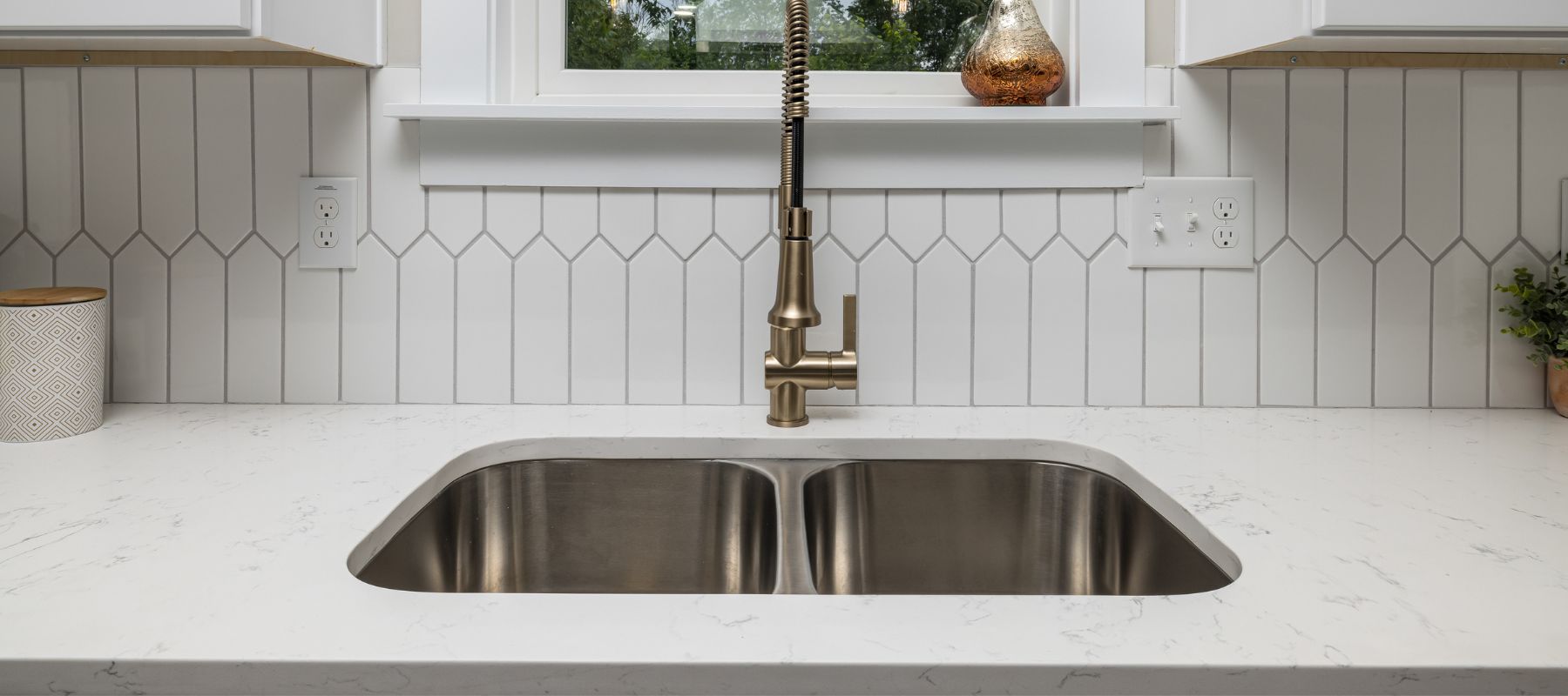 Modern kitchen sink with a gold faucet and white tile backsplash