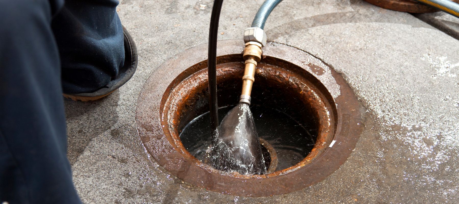 Worker performing hydro jetting by cleaning a drain line with high-pressure water