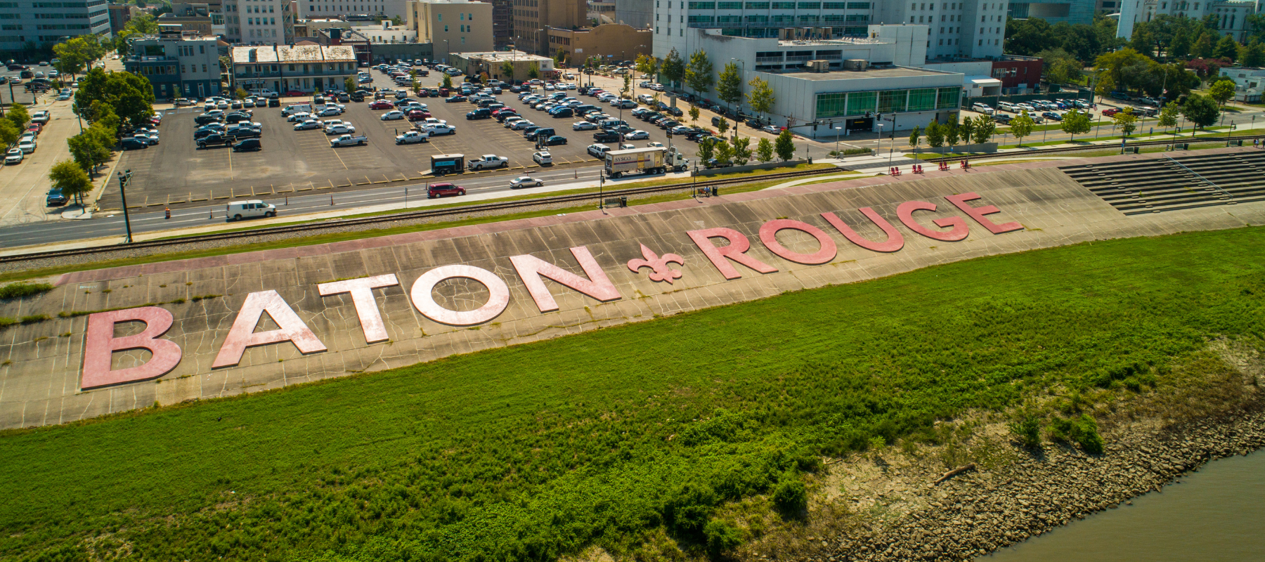 Aerial view of downtown Baton Rouge with large painted letters spelling “Baton Rouge” on a levee near the Mississippi River