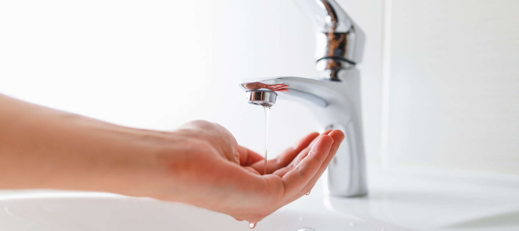 Hand under a bathroom sink depicting low water pressure, possibly a water line repair is needed.