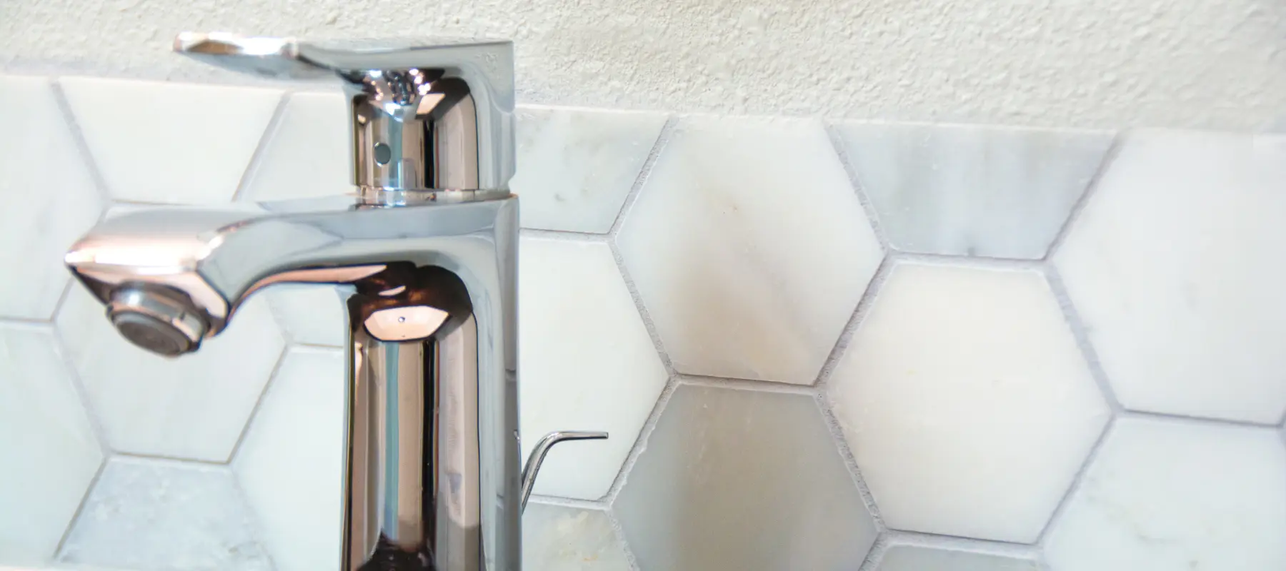 Chrome bathroom sink faucet with tile backsplash, honeycomb pattern.
